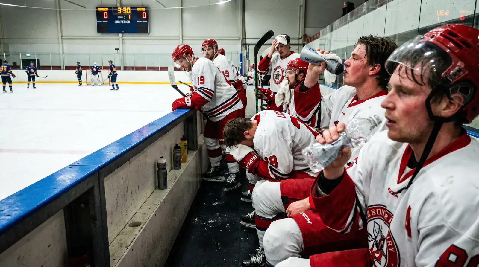Ice hockey players sitting on the bench looking exhausted during a break in play with towels and water bottles visible